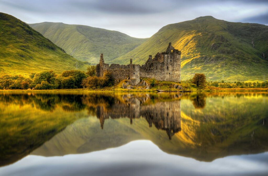 Ein Schloss und die sanfte Hügellandschaft spiegeln sich in perfekter Symmetrie im See